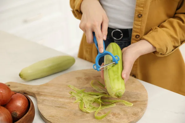 Woman peeling zucchini at kitchen counter, closeup. Preparing vegetable