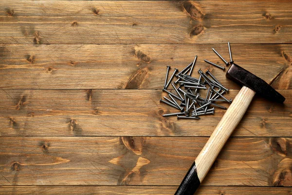 Hammer and metal nails on wooden table, flat lay. Space for text