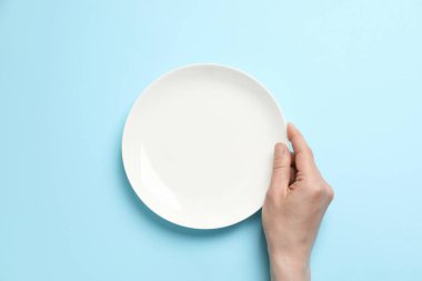 Açık mavi arka planda boş tabak tutan kadının üst görünümü, yakın plan