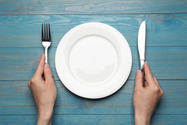 Mavi ahşap masada boş tabak ve çatal bıçak takımı olan bir kadın.