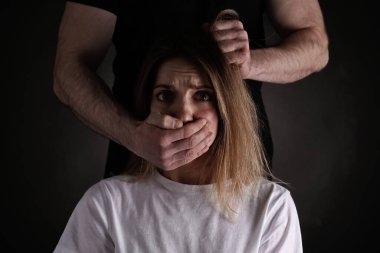 Adam, korkmuş kadını siyah arka planda istismar ediyor. Aile içi şiddet