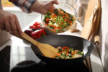 Adam taze sebzeleri kızartma tavasına döküyor, yakın plan.