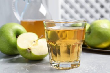 Gri masada bir bardak taze meyve suyu ve elma, yakın plan.