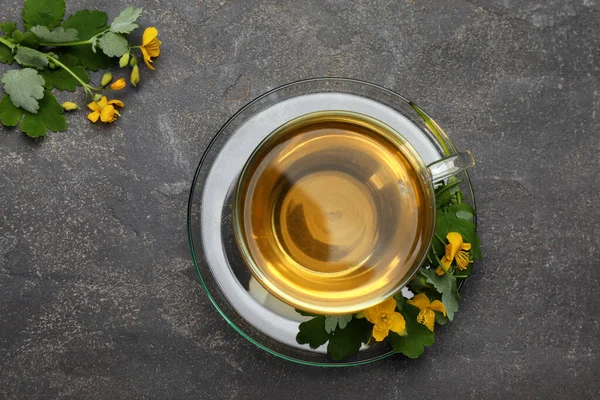 灰色のテーブルに芳香のあるセランディン茶と花のガラスカップ フラットレイ — ストック写真