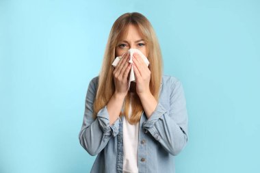 Açık mavi arka planda burnu akan dokuları olan genç bir kadın.