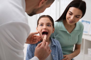 Anne ve kızı çocuk doktorunu hastanede ziyaret ediyorlar. Doktor küçük kızı muayene ediyor.