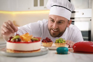 Mutfaktaki lezzetli pastayı dekore eden mutlu profesyonel pastacı.