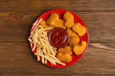 Lezzetli tavuk nugget ve patates kızartması. Tahta masada ketçapla servis ediliyor.