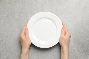 Açık gri masada boş tabağı tutan kadının üst görüntüsü, yakın plan.