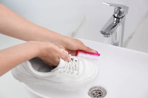 Woman washing shoe with brush under tap water in sink, closeup