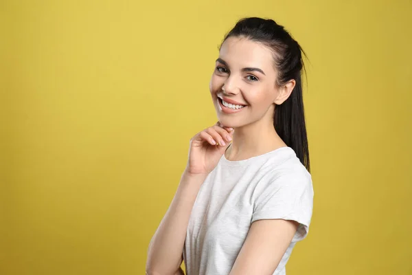 美しい黒い髪と黄色の背景に魅力的な笑顔を持つ幸せな若い女性の肖像 テキストのためのスペース — ストック写真