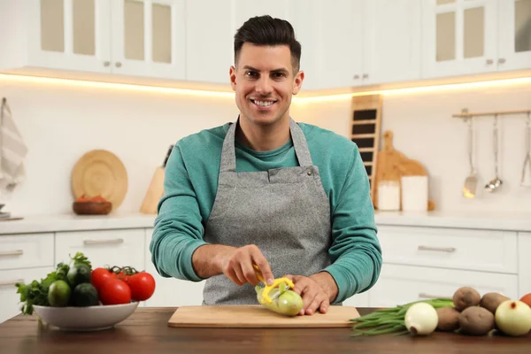 Man peeling zucchini at table in kitchen. Preparing vegetable