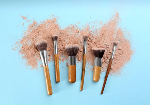 Brushes and scattered face powder on light blue background, flat lay