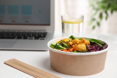Beyaz masadaki dizüstü bilgisayarın yanında tavuk ve sebzeli nefis salata. Metin için boşluk