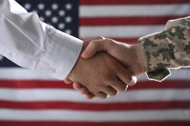 Asker ve işadamı ABD bayrağına karşı el sıkışıyor.