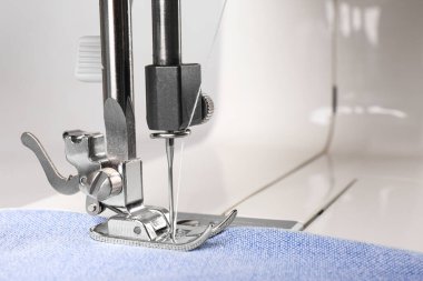 Açık mavi kumaşlı dikiş makinesi, yakın plan.