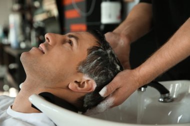 Profesyonel berber müşterinin saçını kuaförde yıkıyor.