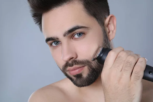 Hombre Joven Guapo Afeitándose Con Trimmer Eléctrico Sobre Fondo Gris — Foto de Stock