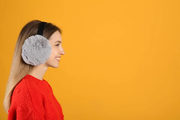 黄色の背景に暖かい耳飾りを身に着けている幸せな女性 テキストのためのスペース — ストック写真