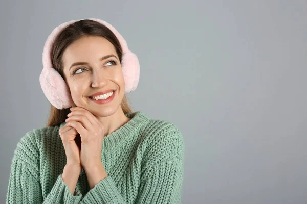 幸せな女性は灰色の背景に暖かい耳飾りを身に着けています テキストのためのスペース — ストック写真