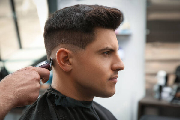 Professional barber making stylish haircut in salon, closeup