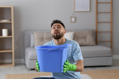 Genç adam evdeki tavandan su sızdırıyor. Çatı tamir servisini arama zamanı.