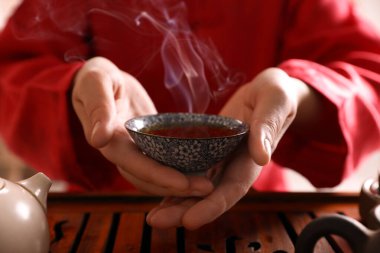 Master offering cup of freshly brewed tea during traditional ceremony at table, closeup clipart