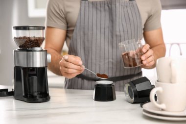 Adam mutfaktaki masada kahve fincanının içine kahve çekirdeği koyuyor, yakın plan.