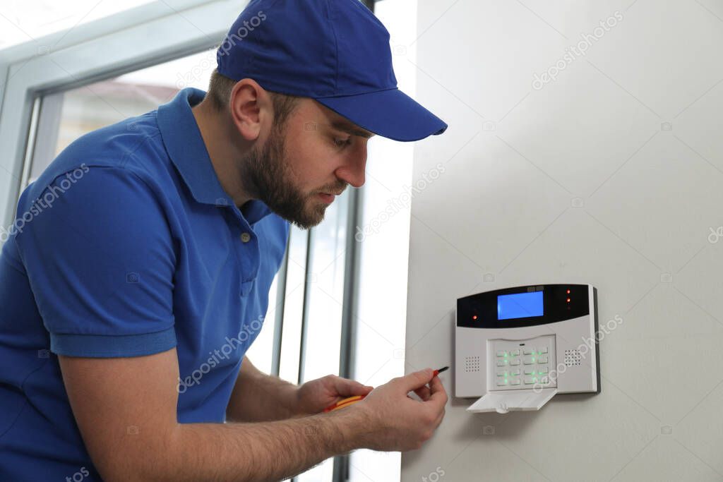 Man installing home security system on white wall in room