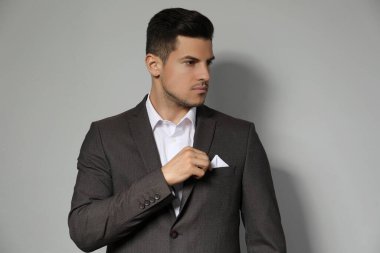 Takım elbisesinin göğüs cebinde açık gri arka planda mendil tamir eden adam.