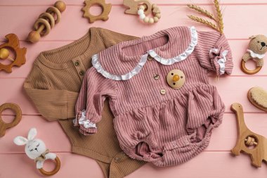 Pembe ahşap arka planda bebek kıyafetleri ve aksesuarları olan düz bir kompozisyon.