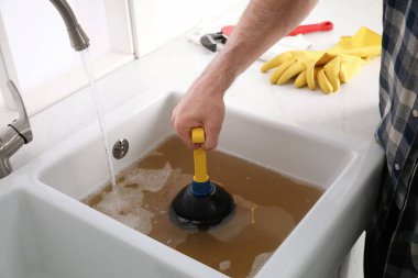 Lavaboyu açmak için lavabo pompası kullanan adam mutfaktaki gideri kapatıyor.