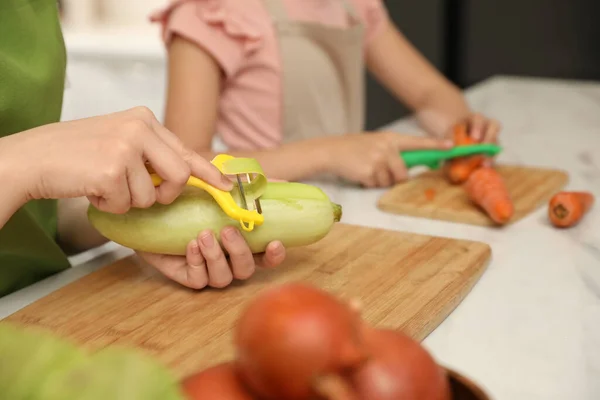Mother and daughter peeling vegetables at table in kitchen, closeup