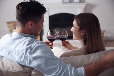Evdeki şöminenin yanındaki koltukta dinlenen şarap kadehli mutlu çift.