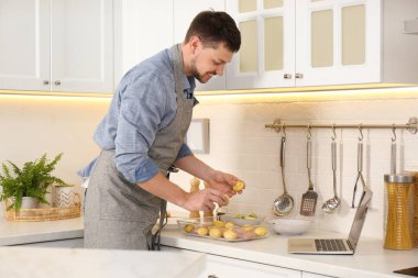 Adam mutfakta dizüstü bilgisayarla yemek pişirirken yemek yapıyor.