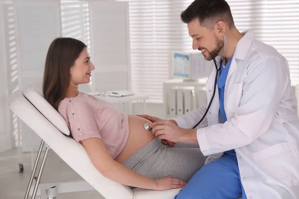 Doctor examining pregnant woman with stethoscope in clinic