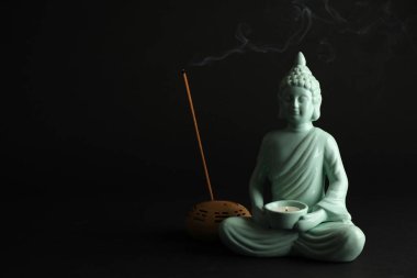 Siyah arka planda yanan mum ve tütsü çubuğu olan güzel seramik Buda heykeli. Metin için boşluk