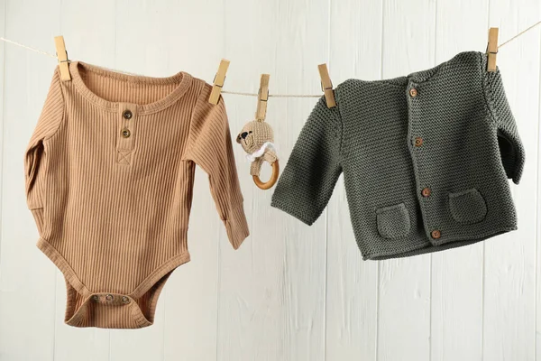 Bebek kıyafetleri ve aksesuarlar beyaz ahşap duvarın yanındaki çamaşır ipinde asılı.