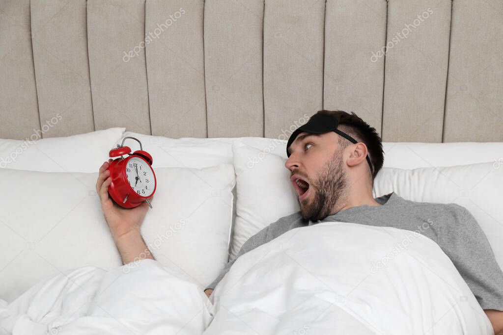 Emotional overslept man with alarm clock in bed, above view. Being late concept