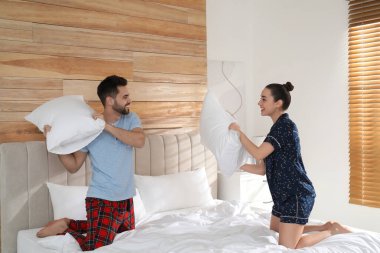 Pijamalı mutlu çift evde yastık savaşı yapıyor.