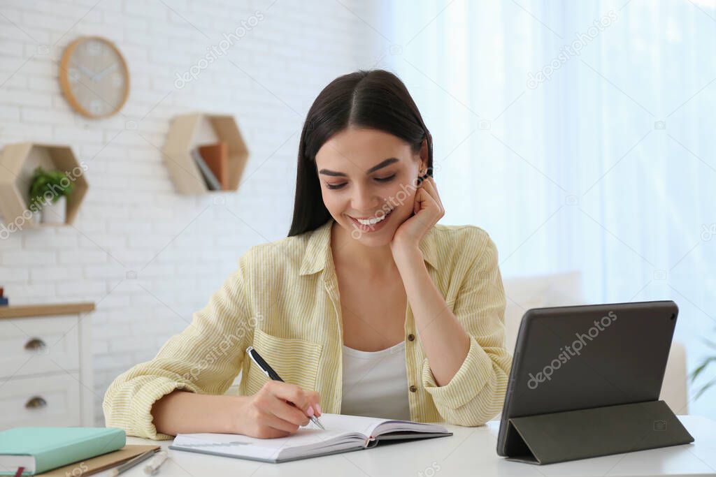 Young woman taking notes during online webinar at table indoors