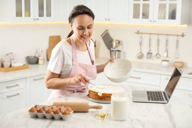 Kadın mutfaktaki dizüstü bilgisayarla çevrimiçi yemek kursunu izlerken pasta yapıyor.