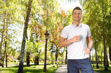 Kulaklıklı genç adam parkta koşuyor, mesaj için yer var. Fitness yaşam tarzı