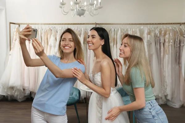 Gelinle fotoğraf çektiren arkadaşlar butikte gelinlik giyiyorlar.