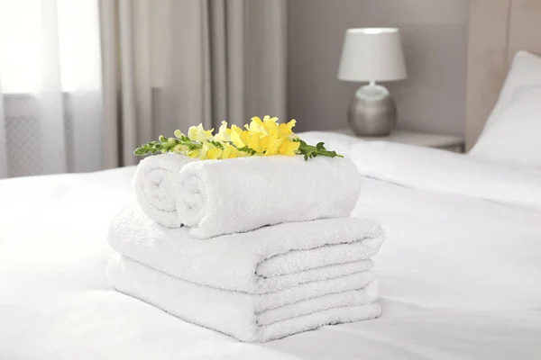 Fresh white towels with flower on bed indoors