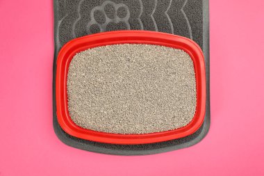 Lastik hasırlar ve kedi kumu tepsisi. Pembe arka planda dolgu malzemesi, üst görünümde.
