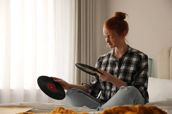 Young woman choosing vinyl disc to play music with turntable in bedroom