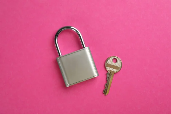 Modern padlock with key on pink background, flat lay