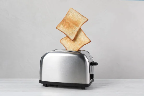 从现代烤面包机上弹出的面包片放在白色的木制桌子上 — 图库照片