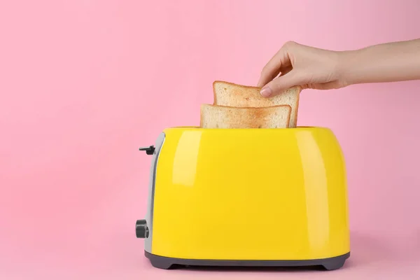 在粉色背景下从黄色烤面包机上取下一片面包的女人 — 图库照片